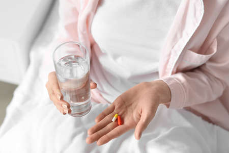 Beautiful young woman taking pills in bedroom, closeupの写真素材