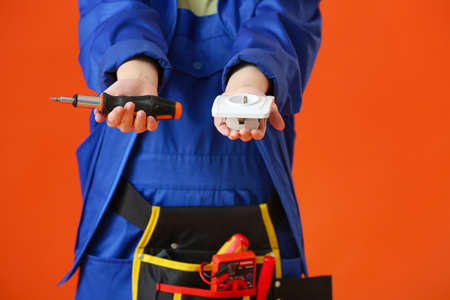 Young female electrician with screwdriver and socket on color backgroundの写真素材