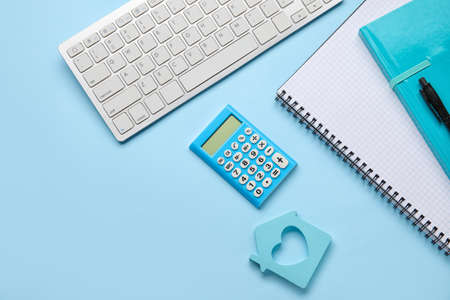 Calculator with model of house, stationery and computer keyboard on color backgroundの写真素材
