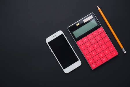 Calculator with mobile phone and pencil on dark backgroundの写真素材