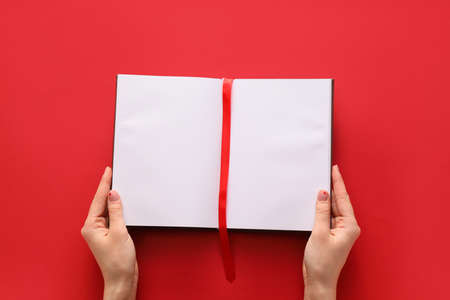 Female hands and blank book with bookmark on color background