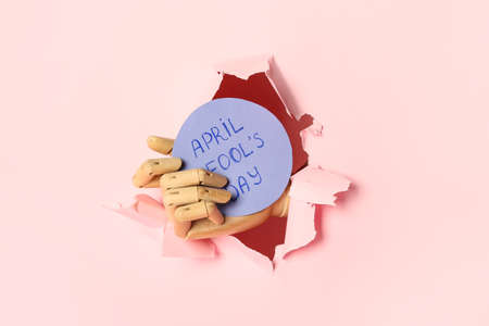Wooden hand and paper sheet with text APRIL FOOL'S DAY visible through hole of torn paper