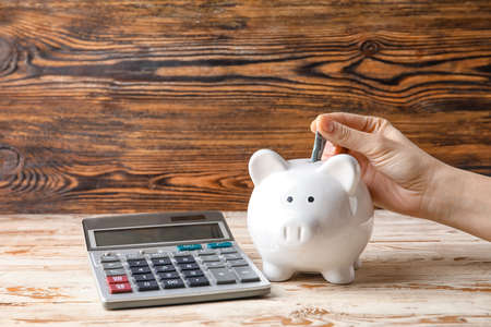 Woman putting money in piggy bank on wooden backgroundの写真素材