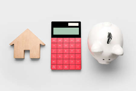 Calculator with piggy bank and house figure on light backgroundの写真素材