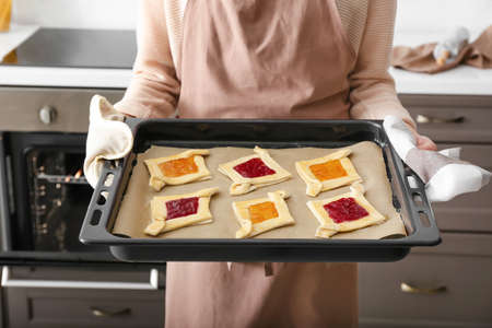 Woman holding baking tray with uncooked Danish pastry in kitchenの写真素材