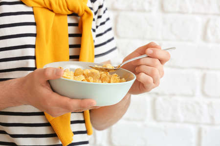 Young man eating cornflakes on brick background, closeup