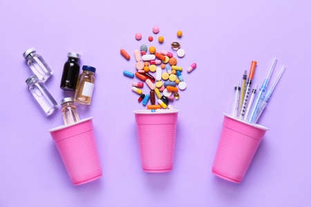 Cups with many pills, ampules and syringes on color backgroundの写真素材