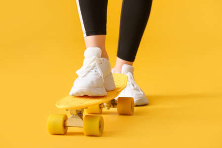 Sporty young woman with skateboard on color background, closeupの写真素材