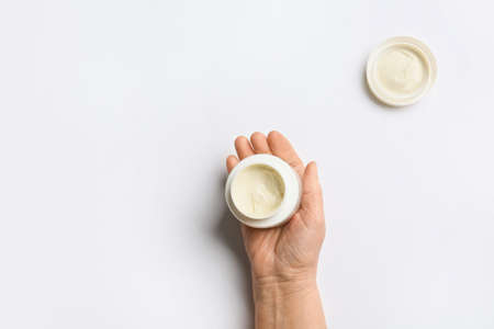 Hand of elderly woman with jar of cosmetic cream on light backgroundの写真素材