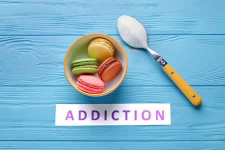 Word ADDICTION and sweet cakes on color wooden background