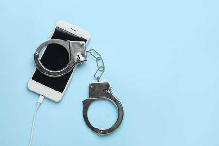Mobile phone with handcuffs on color background. Concept of addiction to gadget