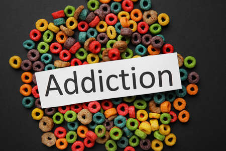 Word ADDICTION and food on dark background