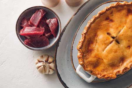 Tasty beef pot pie with ingredients on white background