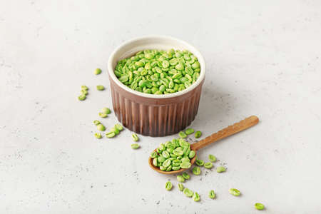 Bowl and spoon with green coffee beans on light backgroundの写真素材