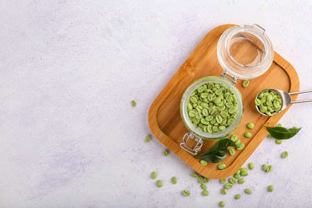 Jar and spoon with green coffee beans on light backgroundの写真素材