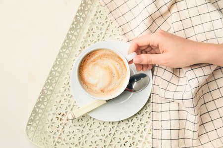Female hand with cup of hot cappuccino on light backgroundの写真素材