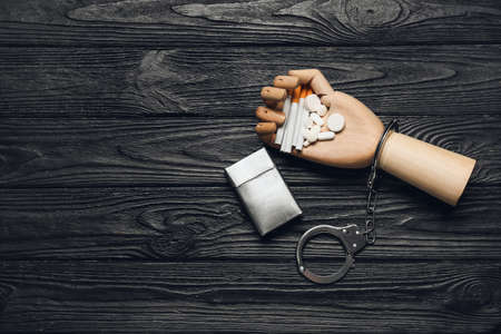 Wooden hand with cigarettes and pills on dark background. Concept of addiction