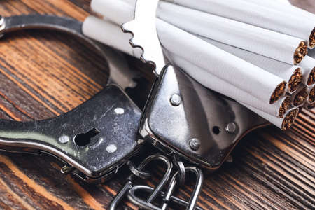 Cigarettes and handcuffs on wooden background, closeup. Concept of addiction