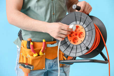 Young electrician with cables on color background, closeup