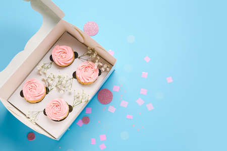 Box with tasty cupcakes and flowers on color backgroundの写真素材