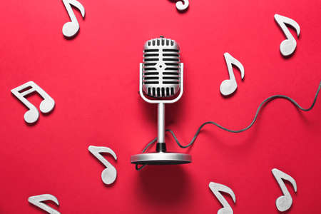 Retro microphone with music notes on color background