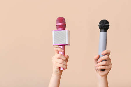 Female hands with modern microphones on color background