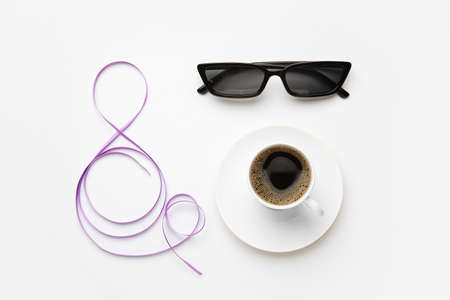 Figure 8 made of violet ribbon, cup of coffee and sunglasses on light background. International...