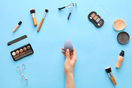 Hand with makeup sponge and cosmetics on color backgroundの写真素材