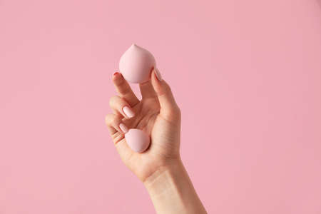 Hand with makeup sponges on color background