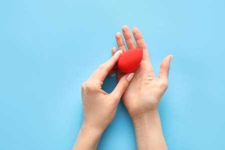 Hands with makeup sponge on color background