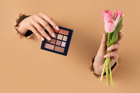 Hands with flowers and cosmetics on color backgroundの写真素材