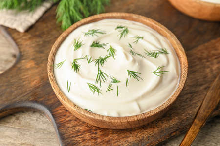 Bowl of tasty sour cream on wooden chopping boardの写真素材