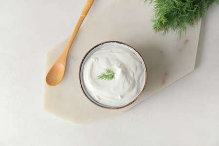 Bowl of tasty sour cream and spoon on light backgroundの写真素材