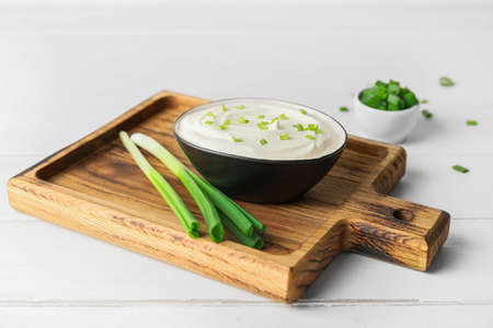 Bowl of tasty sour cream and green onion on white wooden background