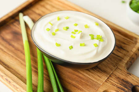Bowl of tasty sour cream and green onion on wooden chopping boardの写真素材
