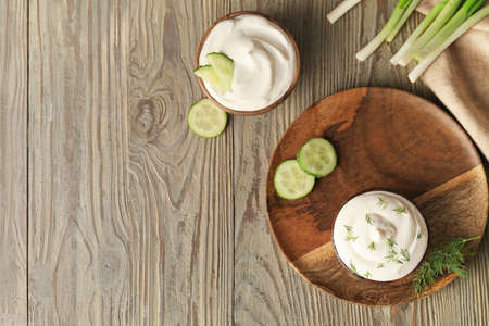 Bowls of tasty sour cream on wooden background