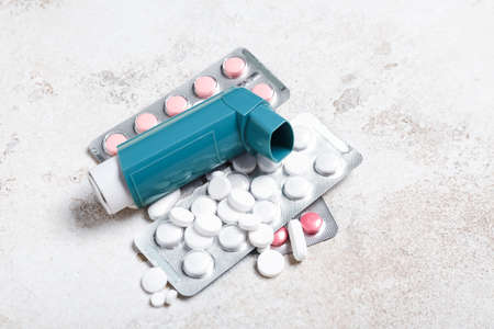 Modern inhaler and pills on light background