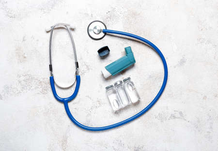 Modern inhaler, ampules and stethoscope on light background