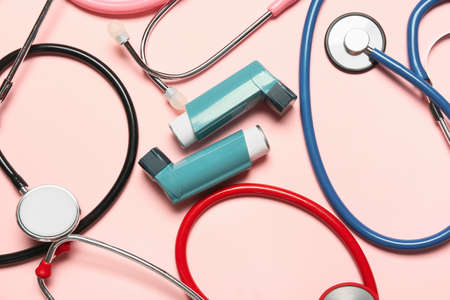 Inhalers and stethoscopes on color background