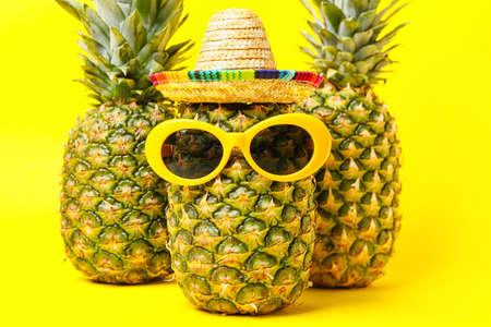 Fresh pineapples with sombrero and sunglasses on color backgroundの写真素材