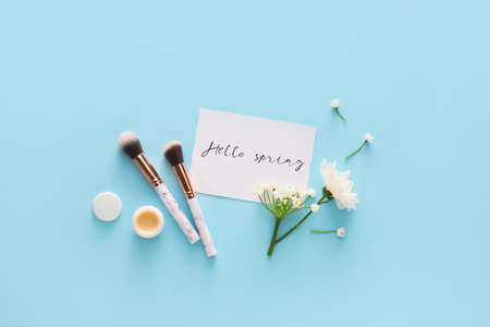 Card with text HELLO SPRING, cosmetics and flowers on color backgroundの写真素材