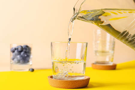 Pouring of water into glass on color background