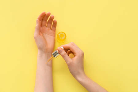 Woman applying essential oil onto her hand against color backgroundの写真素材