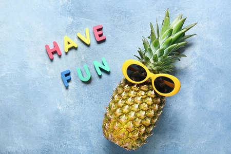 Fresh pineapple with stylish sunglasses and text HAVE FUN on color background