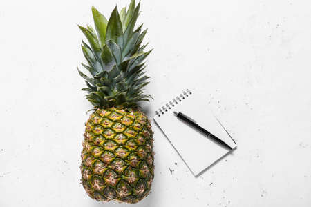 Fresh pineapple with notebook and pen on white backgroundの写真素材