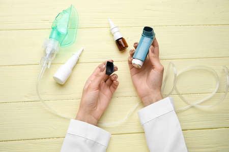 Female doctor with inhaler on color wooden background