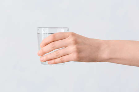 Female hand with glass of water on gray background