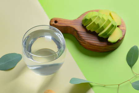 Glass of water and avocado on color background