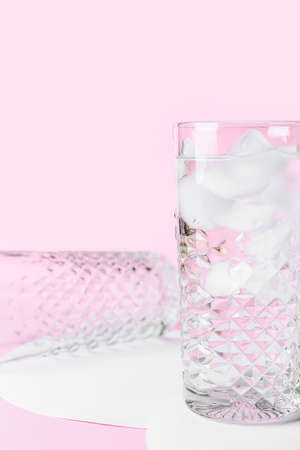 Glasses of water with ice cubes on color background