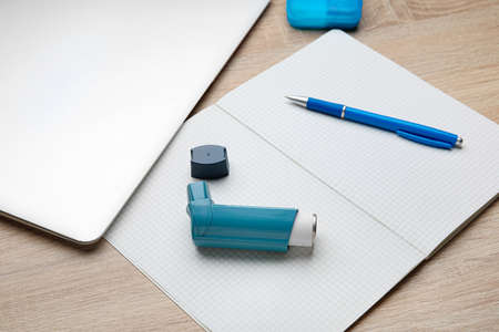 Composition with inhaler, laptop and notebook on light wooden background